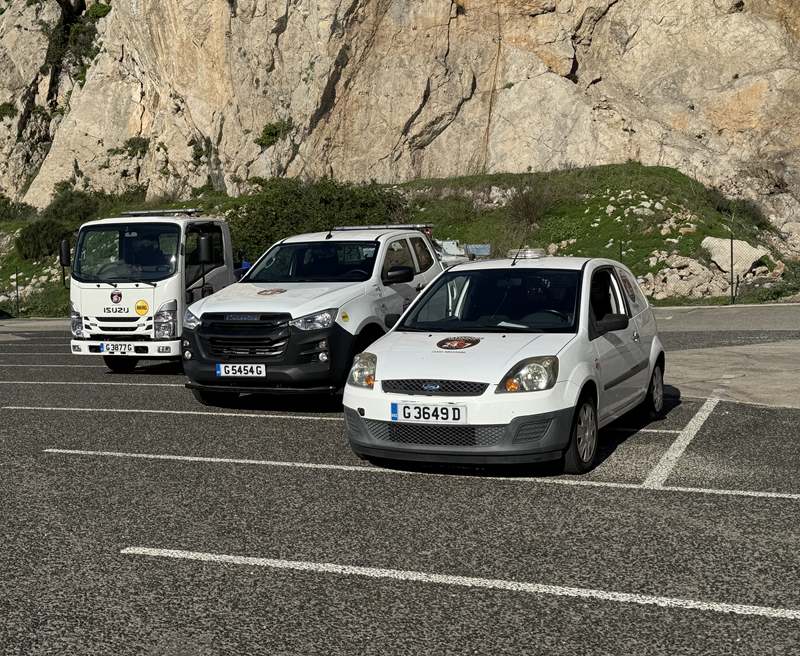 Altimore's flatbed, spec-lift and service van lined up against the Rock face at New Harbours.